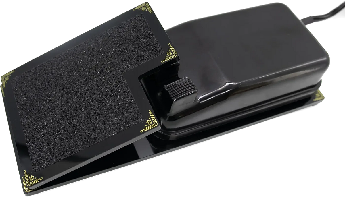 The Foot Controller Adaptor, a black hinged paddle with gold scrollwork corners and an anti-slip pad, cradling an original Singer Featherweight foot pedal