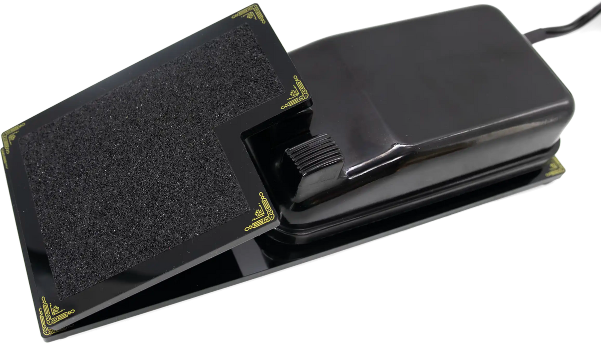 The Foot Controller Adaptor, a black hinged paddle with gold scrollwork corners and an anti-slip pad, cradling an original Singer Featherweight foot pedal.