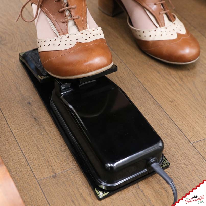 Top-down view of the Foot Controller Adaptor holding the original foot pedal, cord running out the back, a shoe on the paddle.