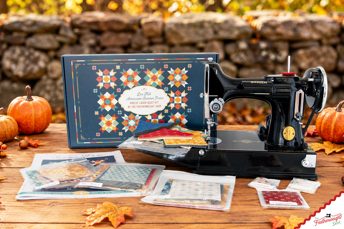 Quilt kit box and a Singer Featherweight on a table by a stone wall