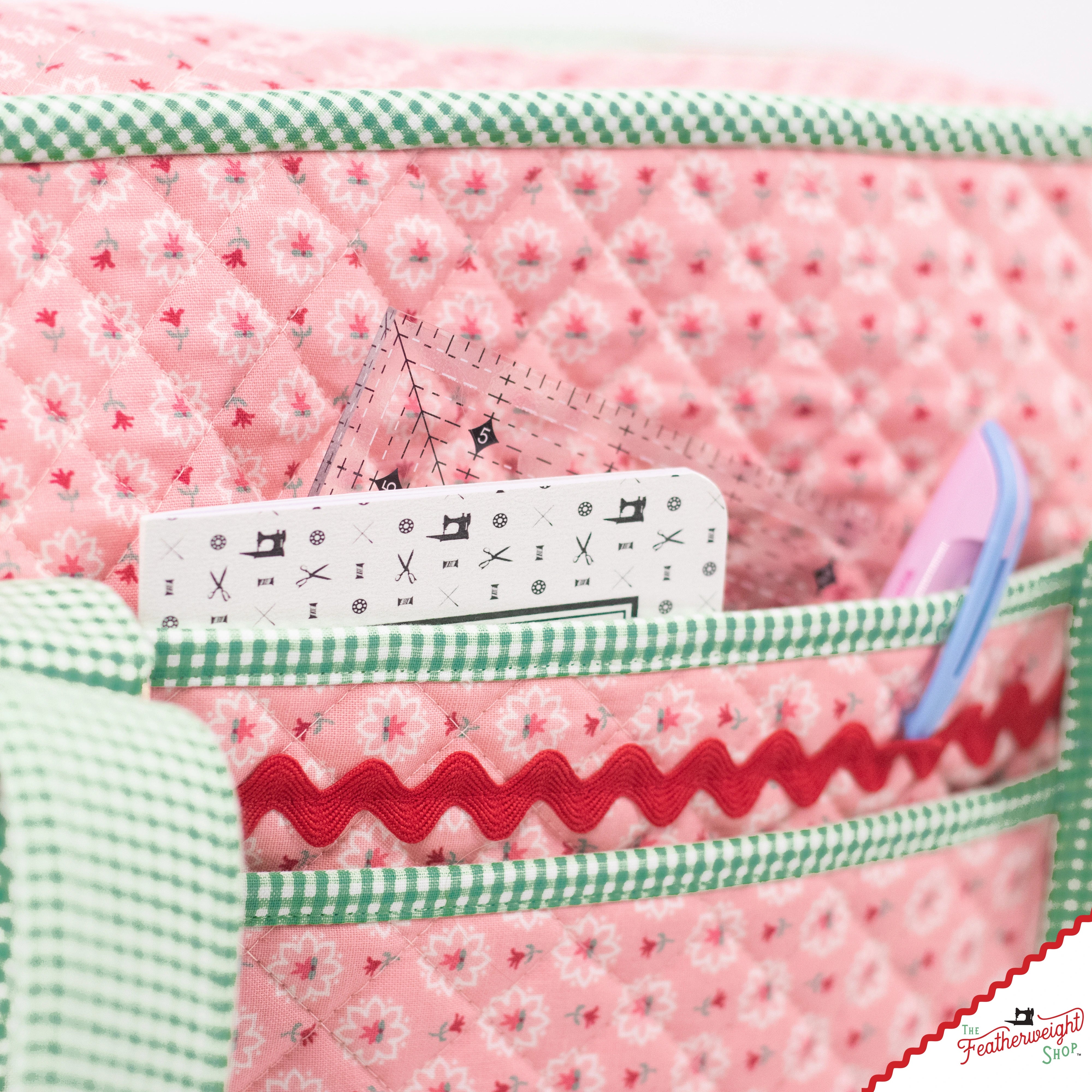 Close view of the front of the Stitcher's Suitcase, where a slip pocket holds a quilting ruler and notebook above a zippered pocket trimmed with red ric rac and green gingham binding.