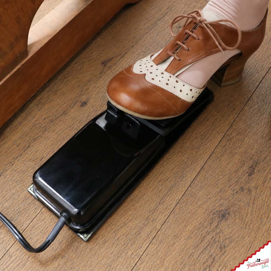 A shoe resting on the Foot Controller Adaptor beside the sewing table, the original foot pedal held underneath