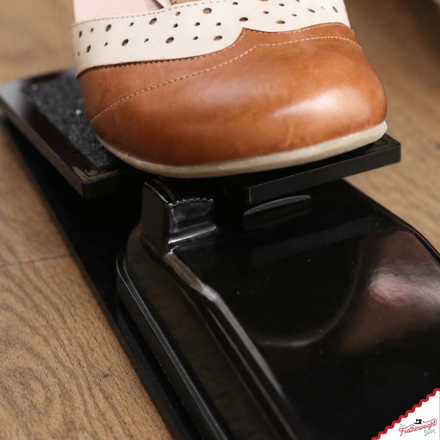 Close view of the adaptor's hinged plate pressing down onto the original foot pedal's ribbed button