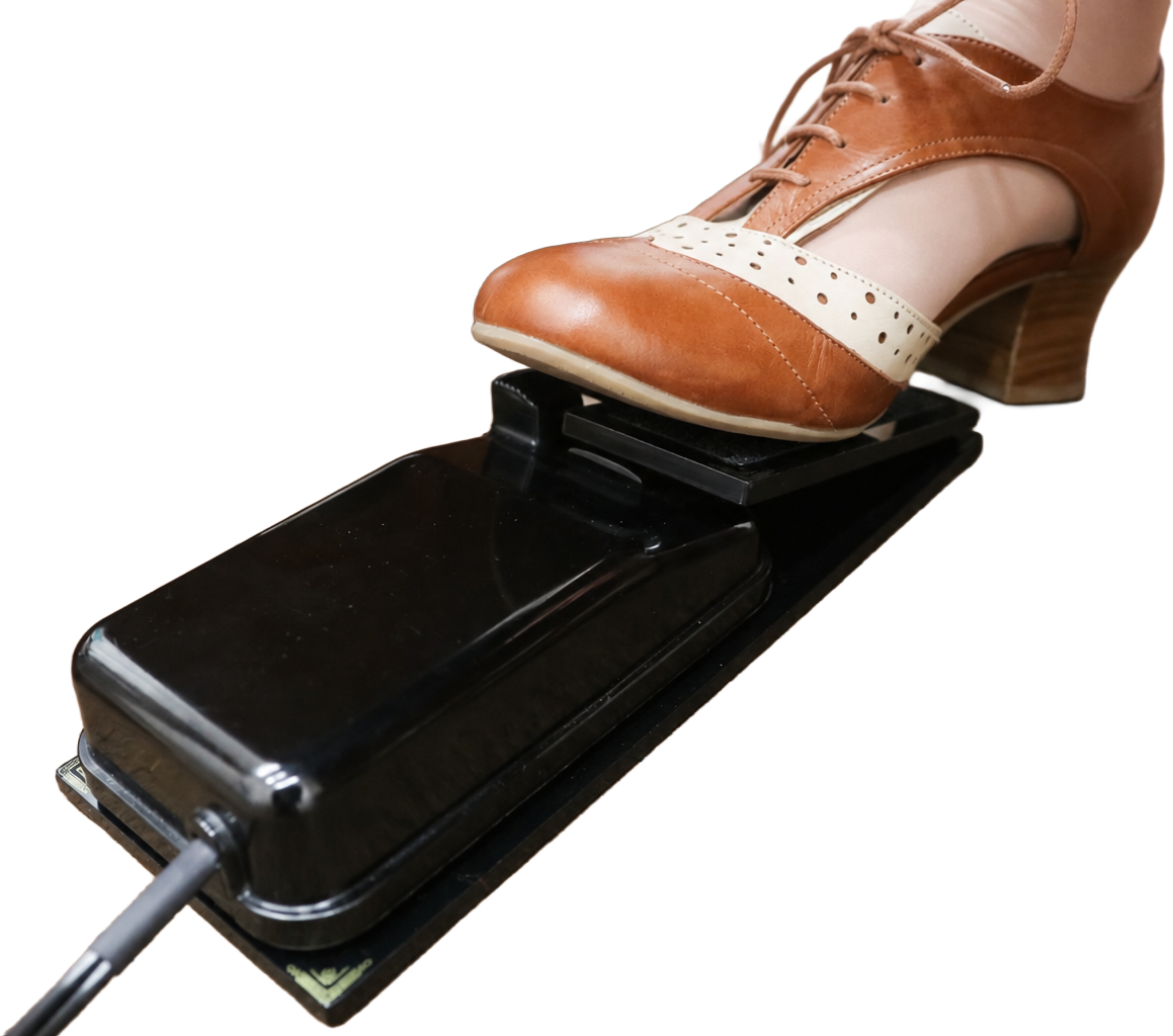 A shoe pressing the Foot Controller Adaptor, the original foot pedal cradled beneath it.