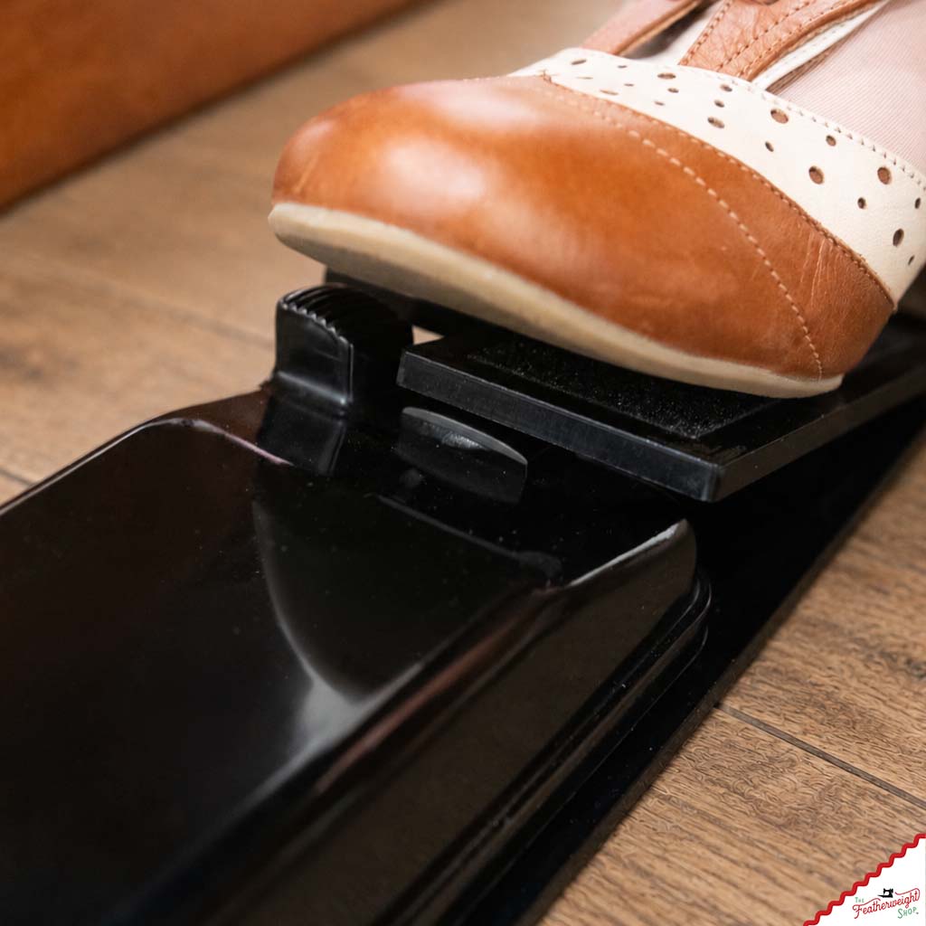 Low side view of the adaptor's paddle hinged over the original foot pedal, the toe of a shoe pressing down.