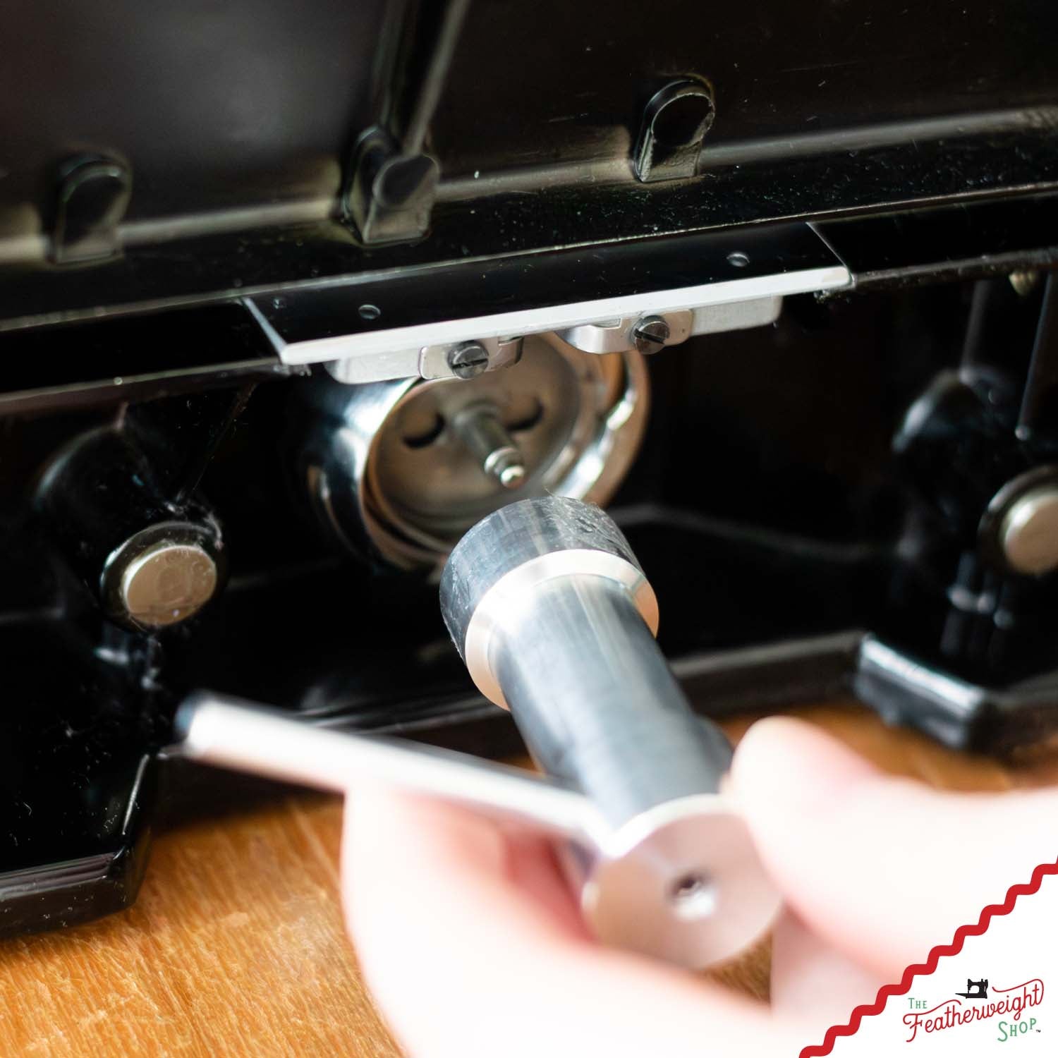 A hand fitting the Thread Jam Removal Tool over the bobbin case base of a black Featherweight
